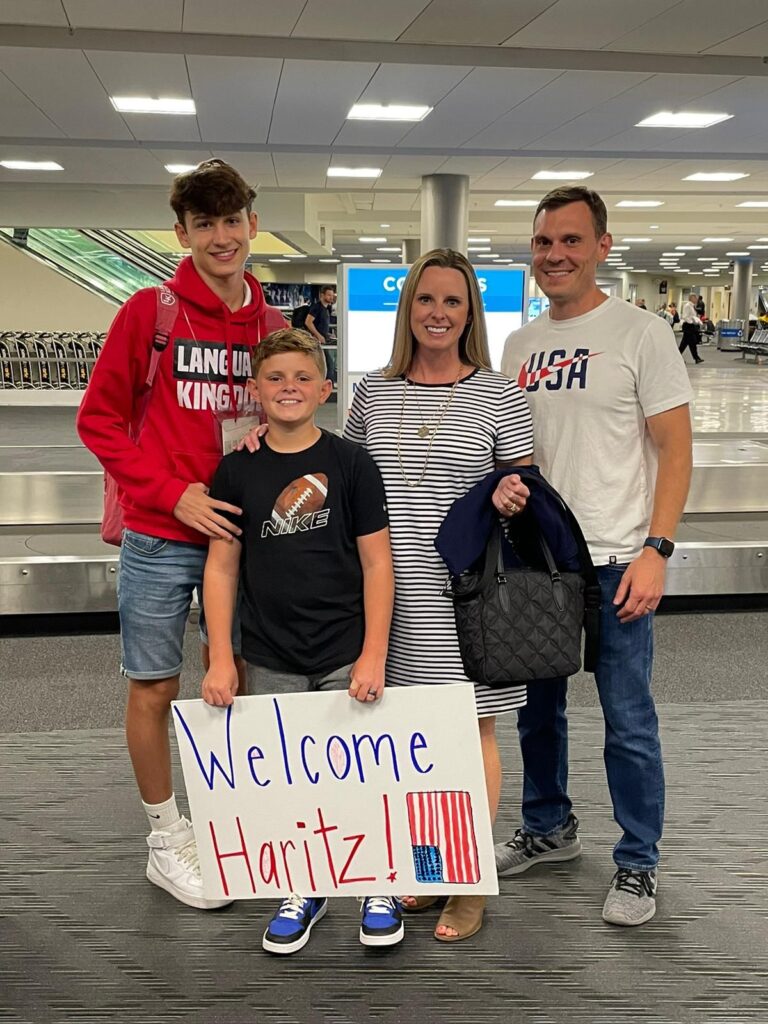 Famiglia ospitante con un cartello di benvenuto agli arrivi dell'aeroporto.