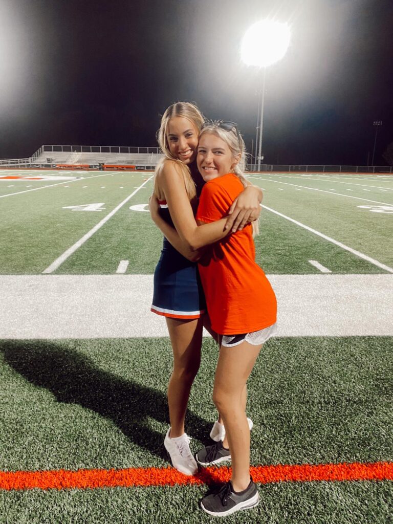 Due cheerleader abbracciate sul campo da football di una high school americana.