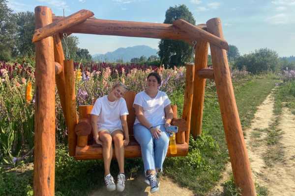 Due persone sedute su un'altalena di legno in un campo fiorito.