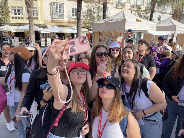 Studentesse si fanno un selfie di gruppo in una piazza di mercato.