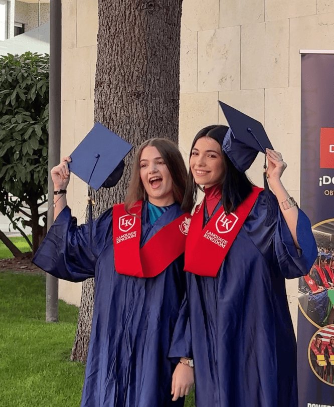 Due studentesse sorridenti alzano il tocco della graduation con la toga del doppio diploma americano.